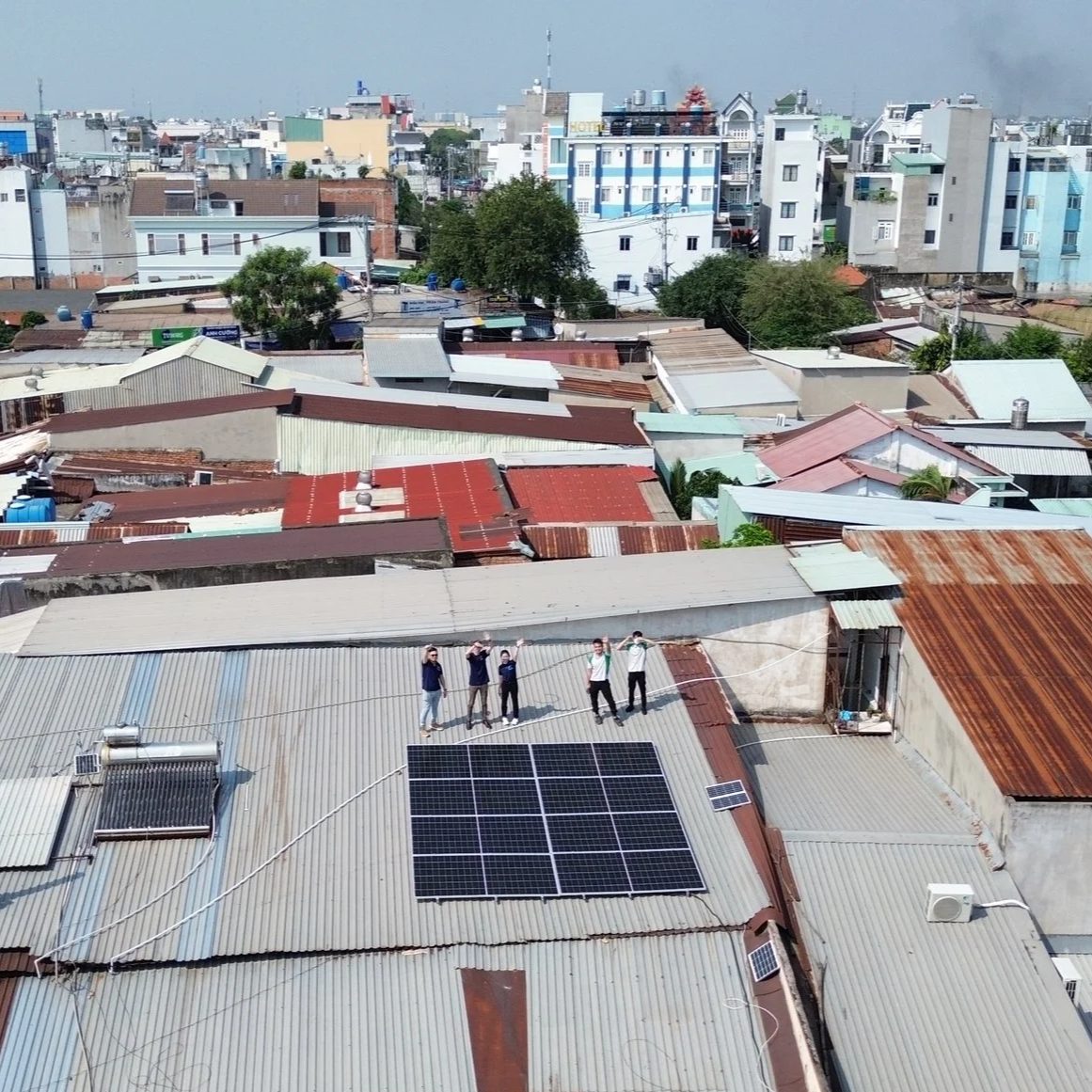 Five team members waving from a corrugated roof in Ho Chi Minh City beside a freshly installed solar array