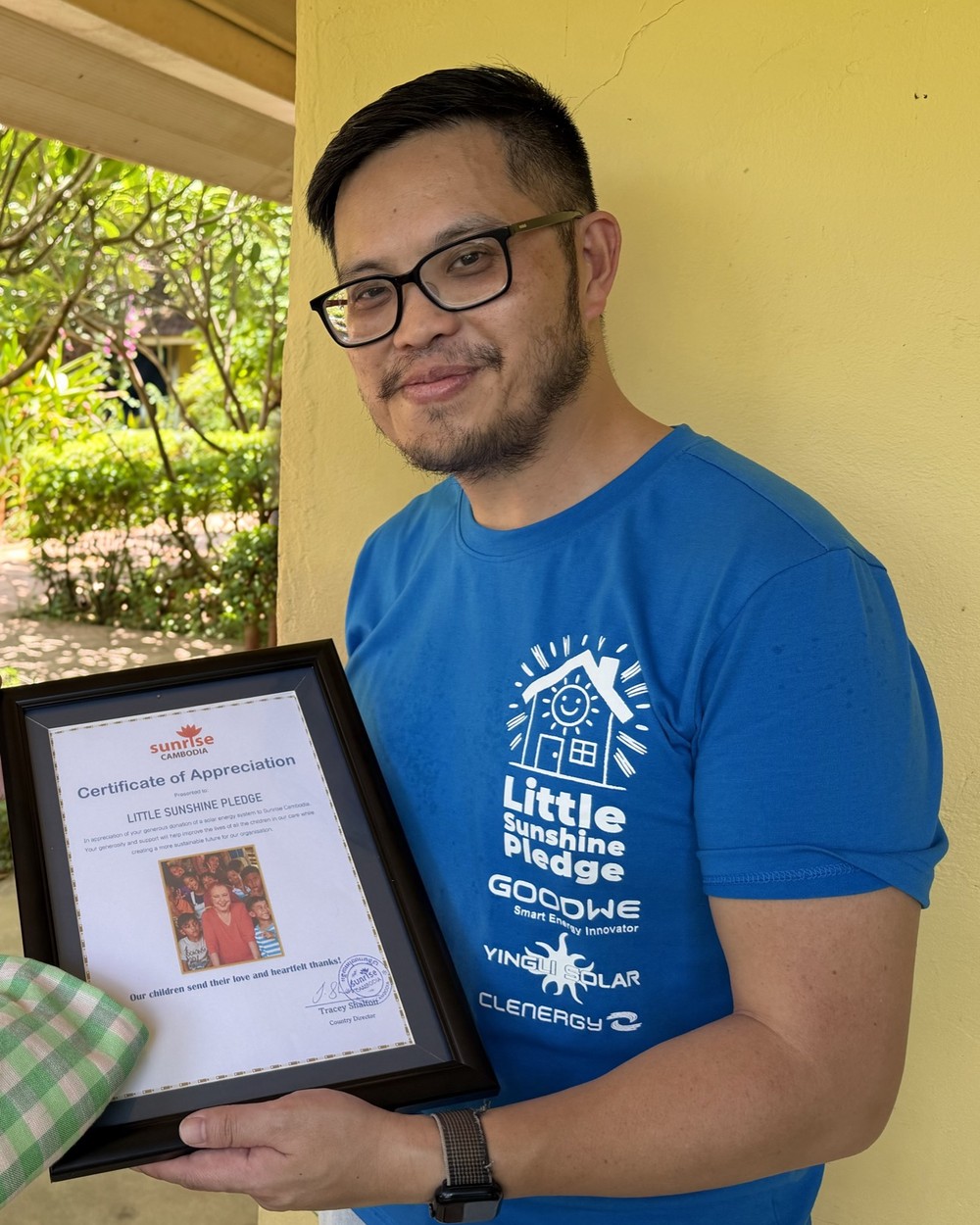 Peter Chang smiling, in a Little Sunshine Pledge shirt, holding a certificate of appreciation